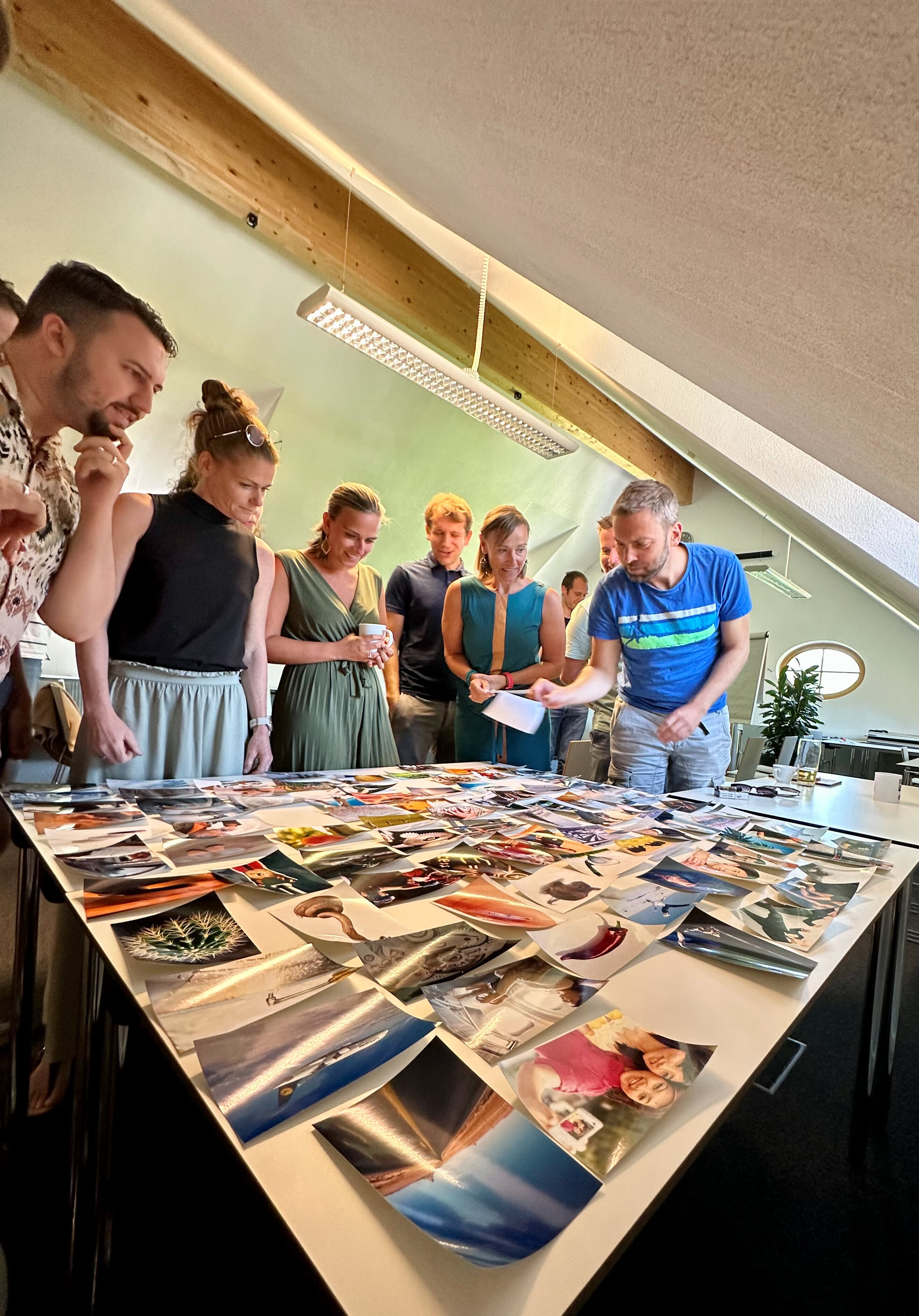 Team betrachtet viele ausgedruckte Fotos auf einem großen Tisch während eines Workshops im hellen Büro.